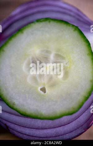 Close-up of a cucumber slice on top of slices of red onion Stock Photo