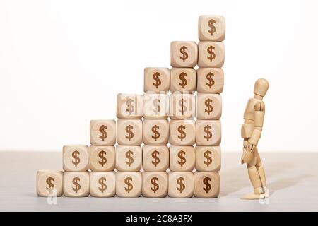 Growth, wealth or richness concept. wooden mannequin looking at a Group of wooden blocks stacked with dollar symbol Stock Photo