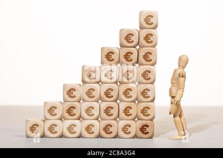 Growth, wealth or richness concept. wooden mannequin looking at a Group of wooden blocks stacked with euro symbol Stock Photo