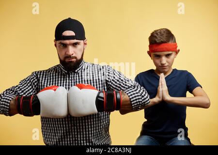 Father and son with boxing gloves doing namaste gesture on yellow background Stock Photo