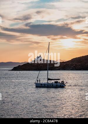 Sailboat on calm sea and orange sky background, Sailing at sunset in the Aegean Mediterranean sea, Greece. Lighthouse at Kea island Stock Photo