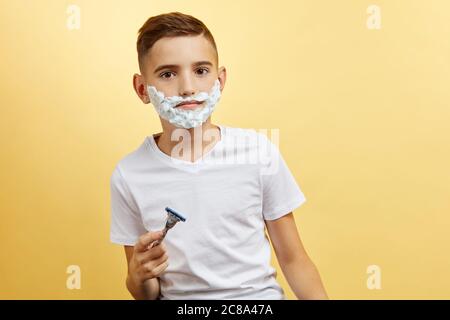 shoking boy do not know how shaving with razor blade in his hand, on yellow background Stock Photo