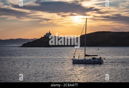 Sailboat on calm sea and orange sky background, Sailing at sunset in the Aegean Mediterranean sea, Greece. Lighthouse at Kea island, reflections on th Stock Photo