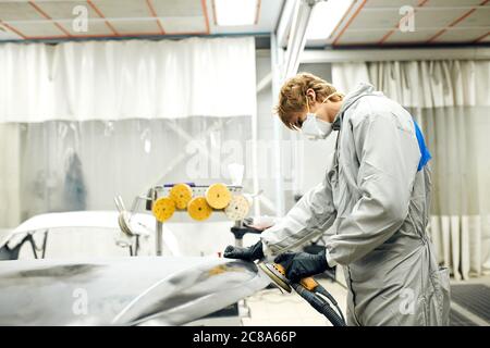 Auto mechanic grinds car part for painting. Car body work auto repair paint after accident Stock Photo