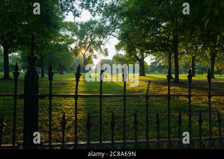 Long shadows through wrought iron fence surrounding La Fayette Park with lens flare aged photo effect at sunset  St Louis Missouri USA Stock Photo