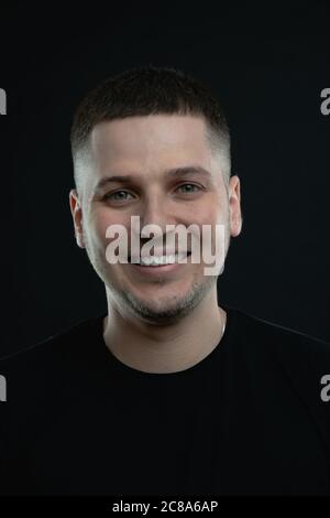Close up portrait of young smiling handsome guy in black t-shirt isolated on black Stock Photo