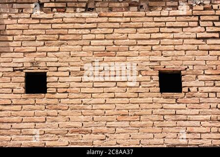 Old wall of an old house, with clay bricks and two small windows. Image for backgrounds or designs Stock Photo