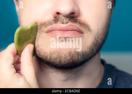 Bearded man is using jade face roller Stock Photo