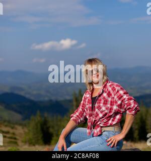 girl in a plaid men's shirt sits on wooden logs high in the carpathian mountains Stock Photo