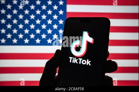 Stone / United Kingdom - July 22 2020: TikTok  logo seen on the silhouette of smartphone hold in a hand with blurred American flag on tha back. Rela p Stock Photo