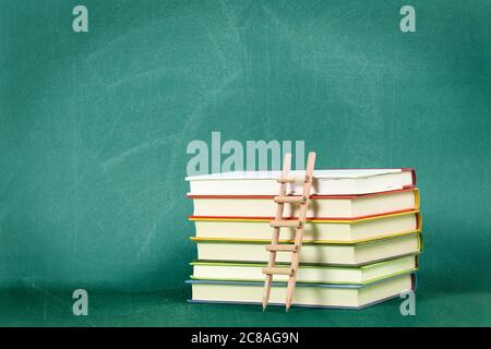pencil ladder on stack of books against green chalkboard, education concept or background Stock Photo