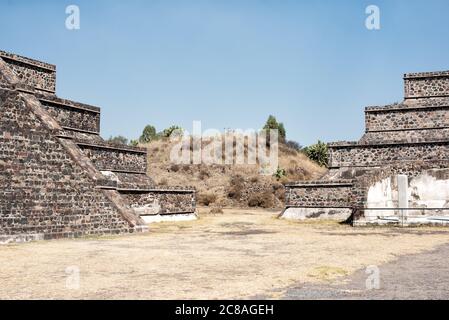 TEOTIHUACAN, Mexico — The expansive view from the plaza in front of the Pyramid of the Moon at Teotihuacan. This vantage point offers a striking perspective of the ancient city's main thoroughfare, the Avenue of the Dead, stretching southward, flanked by smaller pyramids and platforms, with the massive Pyramid of the Sun dominating the eastern skyline. Stock Photo