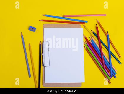 Mockup for drawing and painting, multi-colored pencils and sharpener, empty paper on yellow background Stock Photo