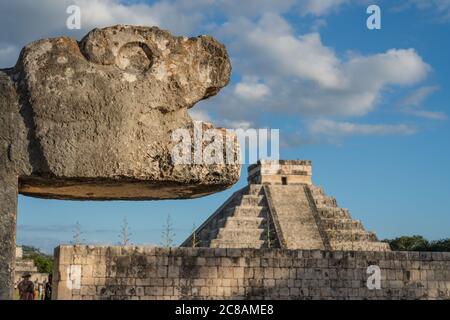 A carved stone jaguar head at the Great Ball Court in the ruins of the great  Mayan city of Chichen Itza, Yucatan, Mexico.  Behind is the Great Pyrami Stock Photo