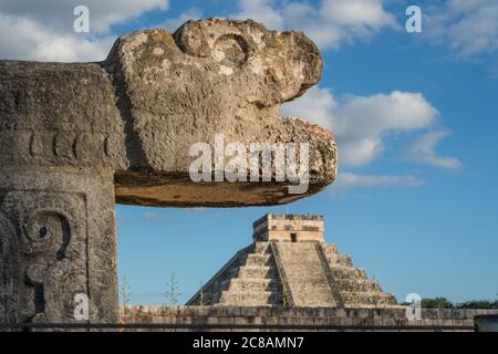 A carved stone jaguar head at the Great Ball Court in the ruins of the great  Mayan city of Chichen Itza, Yucatan, Mexico.  Behind is the Great Pyrami Stock Photo