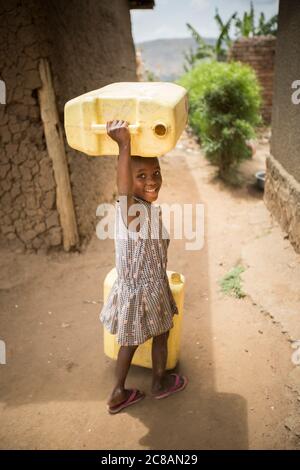 A happy young child fetches water, carrying jerrycans on her head, in Rakai District, Uganda, East Africa. Stock Photo