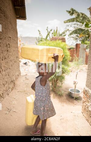 A happy young child fetches water, carrying jerrycans on her head, in Rakai District, Uganda, East Africa. Stock Photo