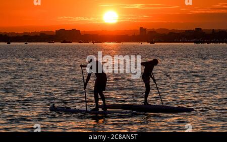 Poole, UK. 22nd July 2020.  Paddleboarders at sunset in Poole Harbour in Dorset viewed from the Sandbanks peninsula.  Credit: Richard Crease/Alamy Live News Stock Photo