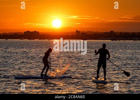 Poole, UK. 22nd July 2020.  Paddleboarders at sunset in Poole Harbour in Dorset viewed from the Sandbanks peninsula.  Credit: Richard Crease/Alamy Live News Stock Photo