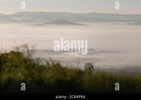 Fog envelops a valley beneath rolling hills and communities of Lyantonde District, Uganda, East Africa. Stock Photo