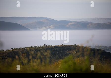 Fog envelops a valley beneath rolling hills and communities of Lyantonde District, Uganda, East Africa. Stock Photo