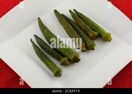 Soy sauce sesame flavored dried okra chips on white snack plate on red tablecloth Stock Photo