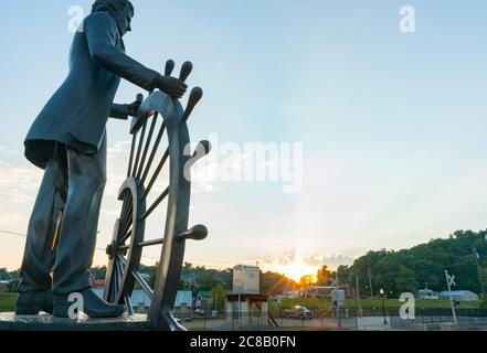 Hannibal USA - September 3 2015; Bronze public art statue of man at wheel of river boat on Glascock's Landing looking over Mississippi River in histor Stock Photo