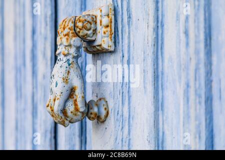 Europe, France, Dordogne, Hautefort. A rusted metal door knocker in the shape of a hand on a blue door in the town of Hautfort. Stock Photo