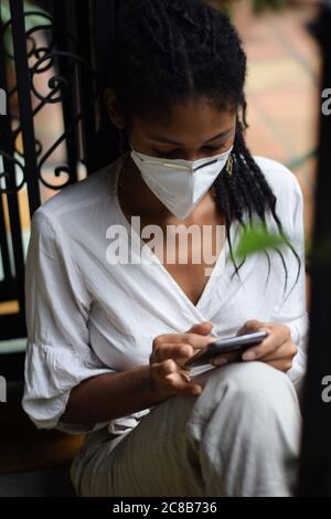 Young black woman in face mask using a smartphone Stock Photo