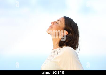 Side view portrait of a satisfied adult woman breathing fresh air standing on a beach in summer Stock Photo