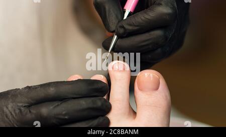 Process pedicure close up in a fashionable spa salon, unrecognizable people. French pedicure, white gel polish Stock Photo