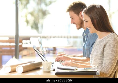 Happy entrepreneurs typing on their laptops working sitting in a coffee shop table Stock Photo