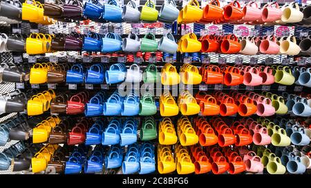 Rows of colorful mugs hanging on the rack for sale in a supermarket, Handcrafted pottery, teapots and dishes for sale Stock Photo