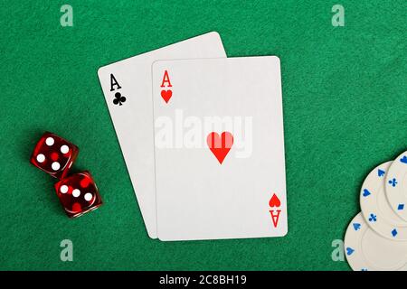 two aces, red dice and poker chips on green felt Stock Photo