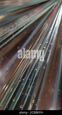 Soft focus to small shiny drops on dark metallic ribbed texture of glossy rays blurred background. Blurry abstract backdrop with diagonal lines and co Stock Photo