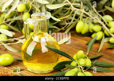 jug of olive oil and olive tree branches on old wooden table Stock Photo