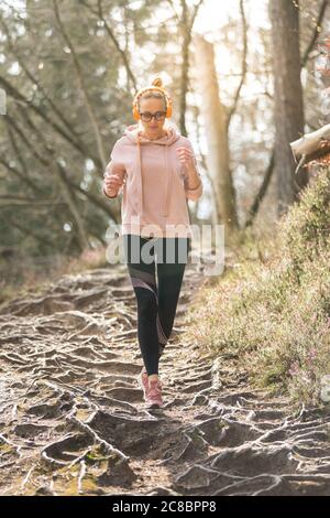 Active sporty woman listening to the music while running in autumn fall forest. Female runner training outdoor. Healthy lifestyle image of young