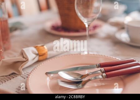 Festive table setting in pastel colored plate and cutlery. Elegant dinner party with flower and wine glasses, natural light Stock Photo