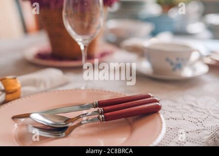 Festive table setting in pastel colored plate and cutlery. Elegant dinner party with flower and wine glasses, natural light Stock Photo