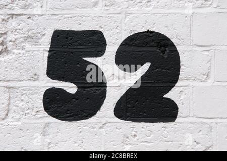 A Close Up Of The Number 52 Hand Painted In Black Paint On A White Painted Brick Wall Stock Photo