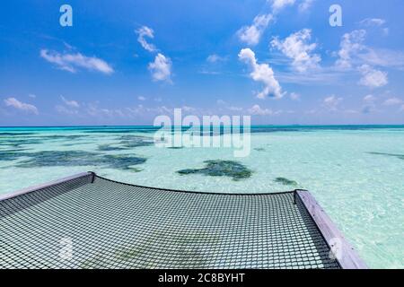 Empty over water hammock in the middle of tropical lagoon in Maldives. Luxury travel vacation concept. Seascape view from luxurious resort Stock Photo