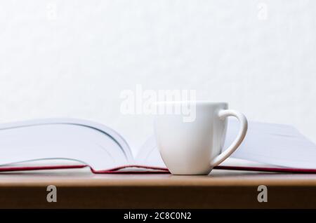 Red hardcover books and white coffee cup or mug with hot beverage on wooden table or desk against white wall, indoors, literature, library Stock Photo
