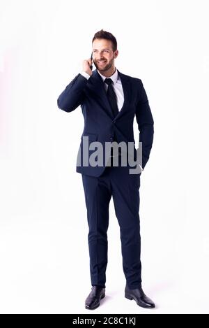 Full length shot of handsome businessman wearing suit and talking with somebody on his mobile phone while standing at isolated white background. Stock Photo