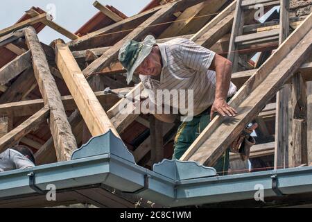 Zrenjanin, Serbia, July 22, 2020. A master works on the roof of a private house to replace the roof tile. He is part of the team that does it. It curr Stock Photo