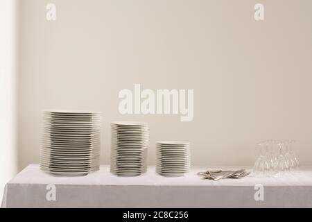 Stacks of plates cutlery and wineglasses on table Stock Photo