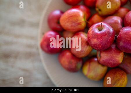 Fresh red apples in a white bowl over wooden table top, soft artistic light Stock Photo