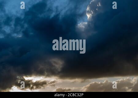 Dark stormy clouds roll across the sky with bright white sunlight shining through at the bottom Stock Photo