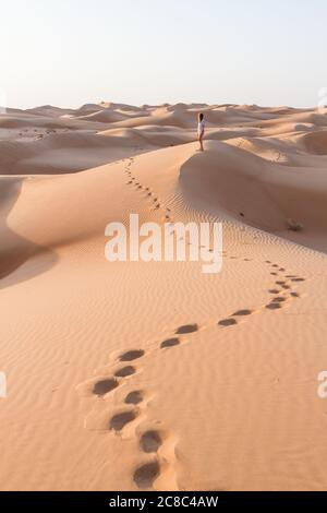 Blonde female Caucasian traveler leaving footprints in sand dunes when walking in dessert in Oman Stock Photo