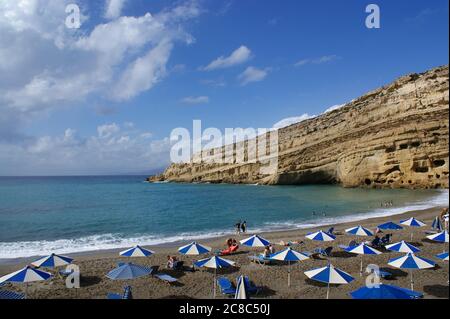 Matala, Crete / Greece / October 15 2010 : Holiday makers relax in the sun at the beach at the charming village of Matala, Crete.  In the background, Stock Photo