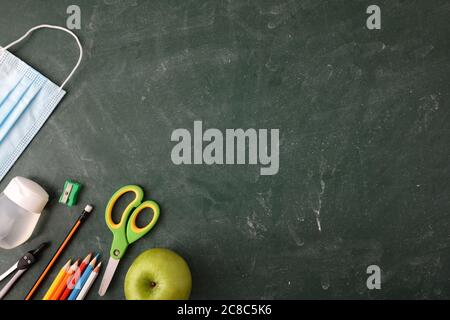 School educational supplies and covid-19 protection elements on green blackboard. Top view. Stock Photo